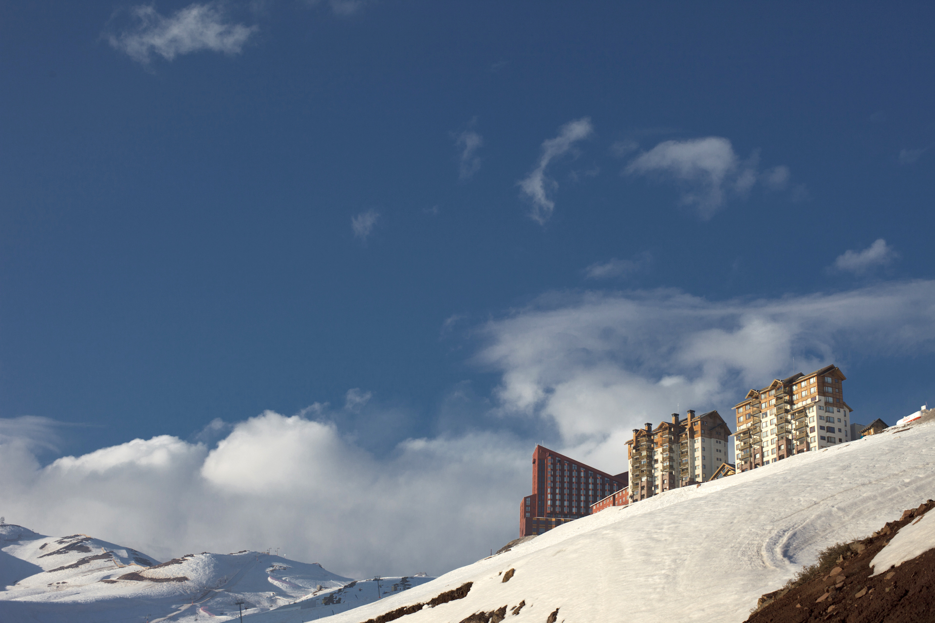 Здания Valle Nevado на заснеженном склоне под голубым небом